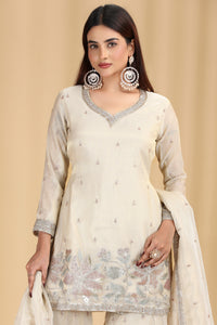 Woman wearing a cream-colored embroidered outfit with a beige background