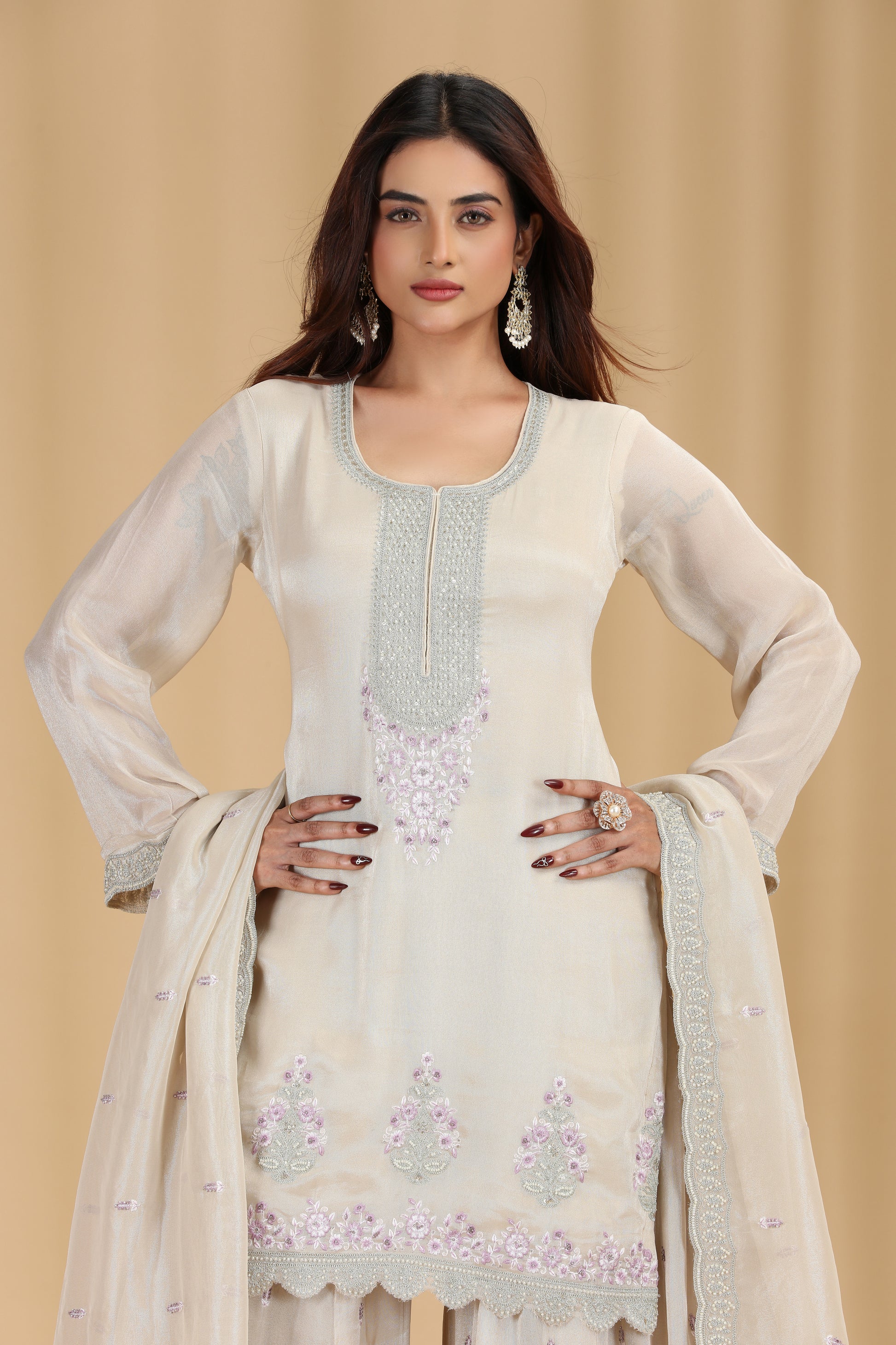 Woman wearing a cream-colored embroidered traditional outfit on a beige background