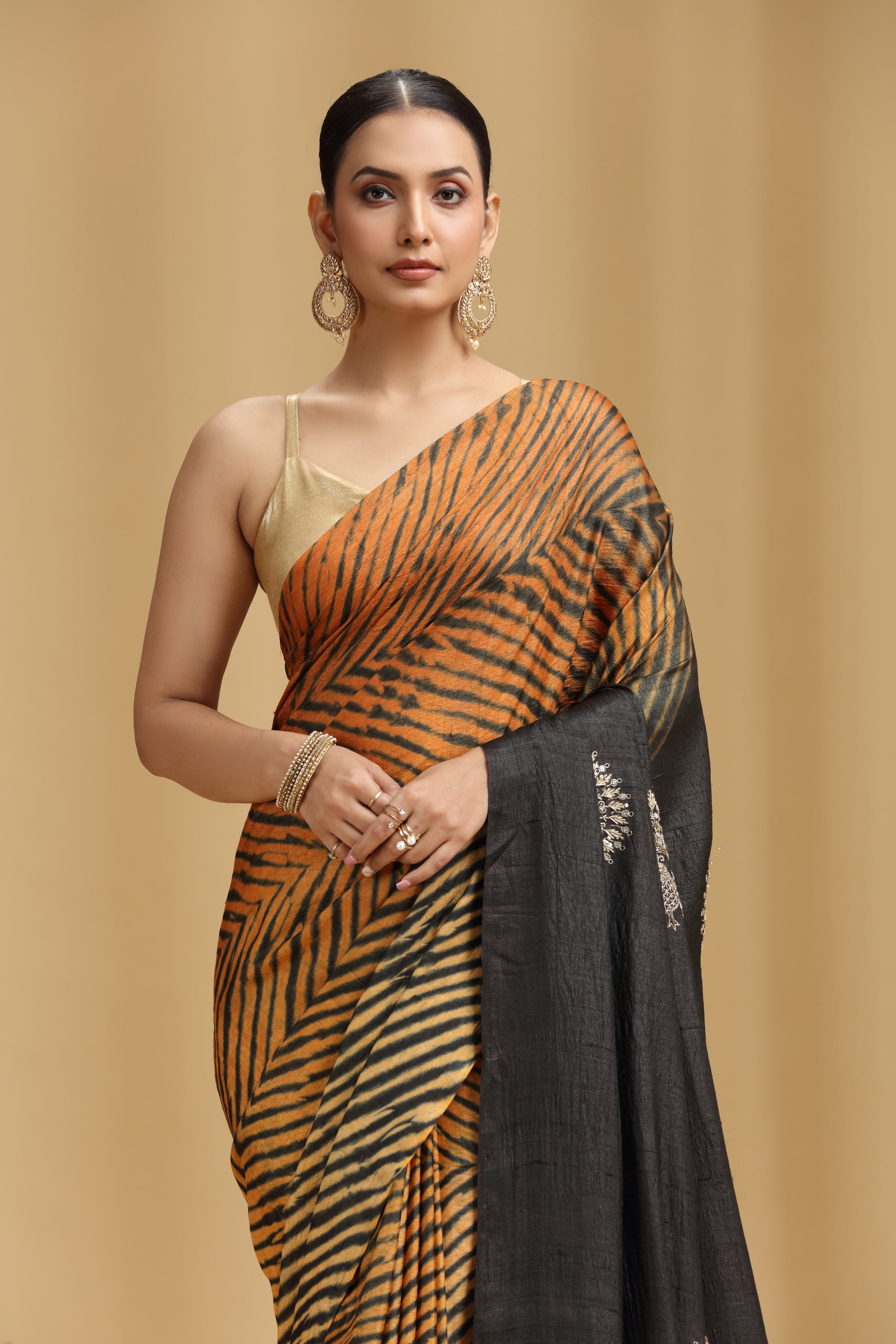 Woman wearing a black and orange saree with a beige background