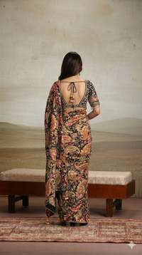 Woman in a floral black saree standing in front of a textured wall.