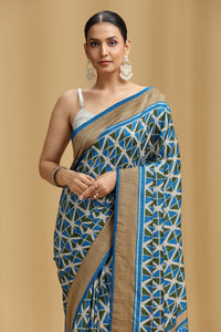 Woman wearing a blue and white patterned saree with a beige border on a beige background