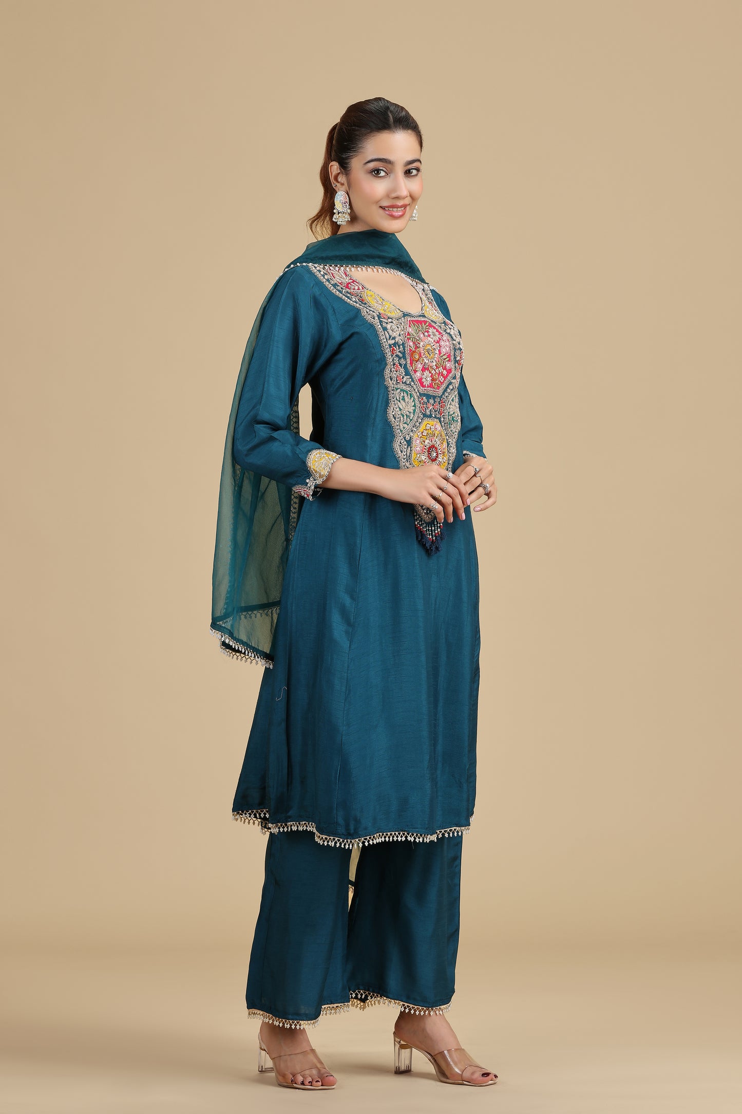 Woman wearing a teal embroidered outfit on a beige background