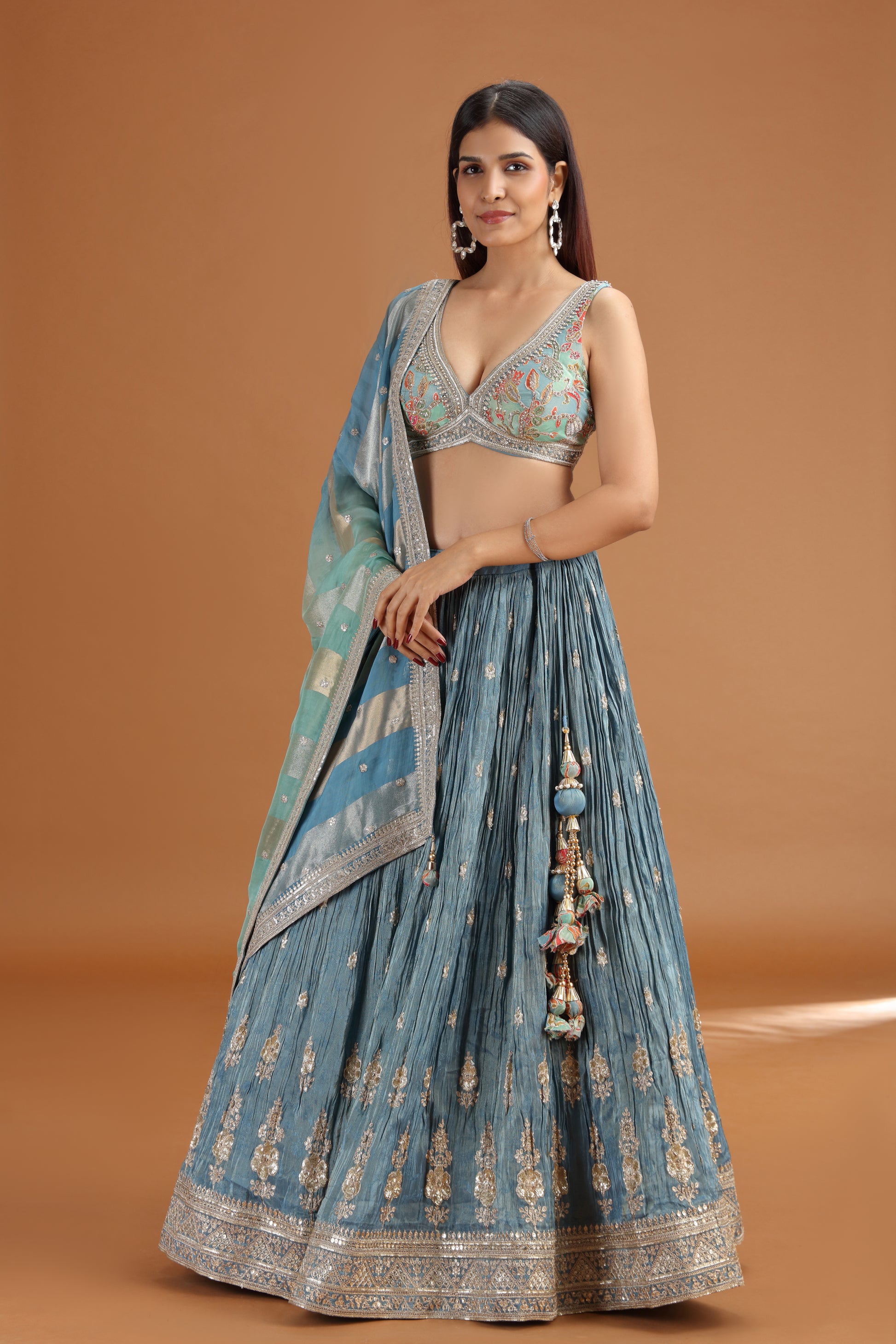 Woman wearing a blue embroidered traditional lehenga with a brown background
