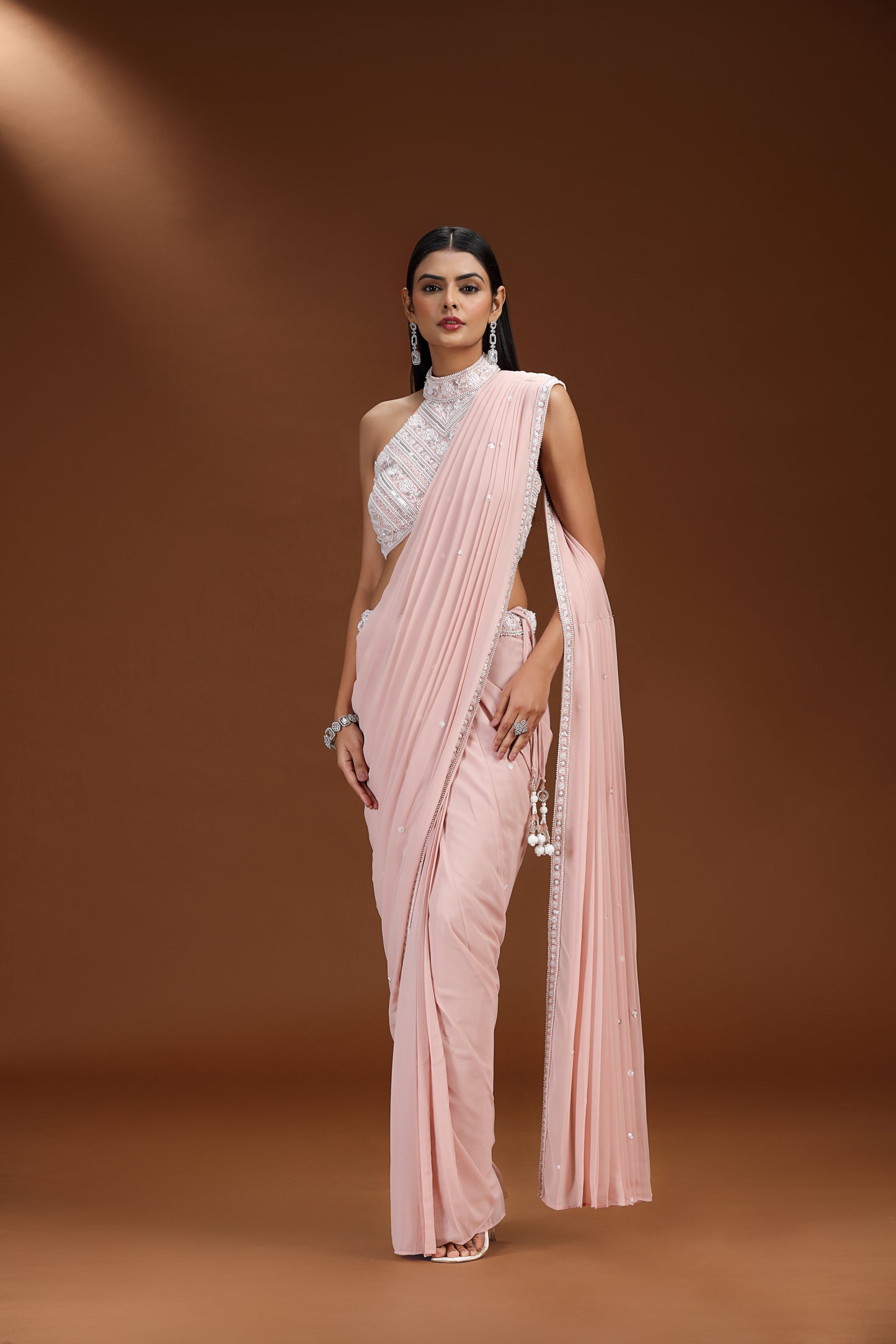 Woman wearing a light pink saree with a white blouse against a brown background
