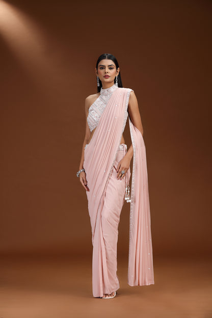 Woman wearing a light pink saree with a white blouse against a brown background