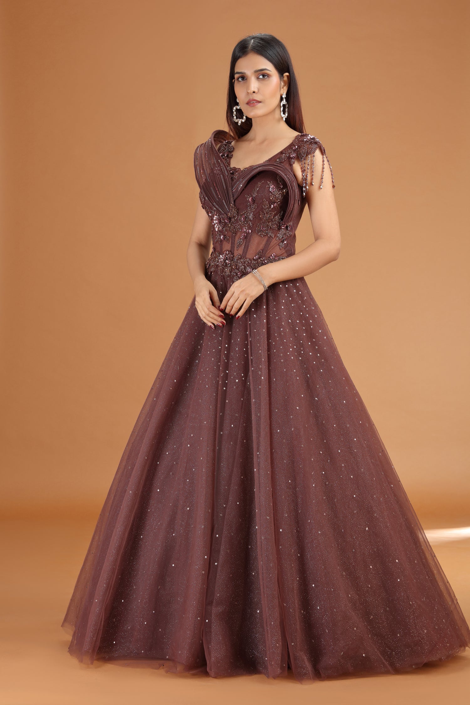 Woman wearing a brown evening gown with intricate details on an orange background