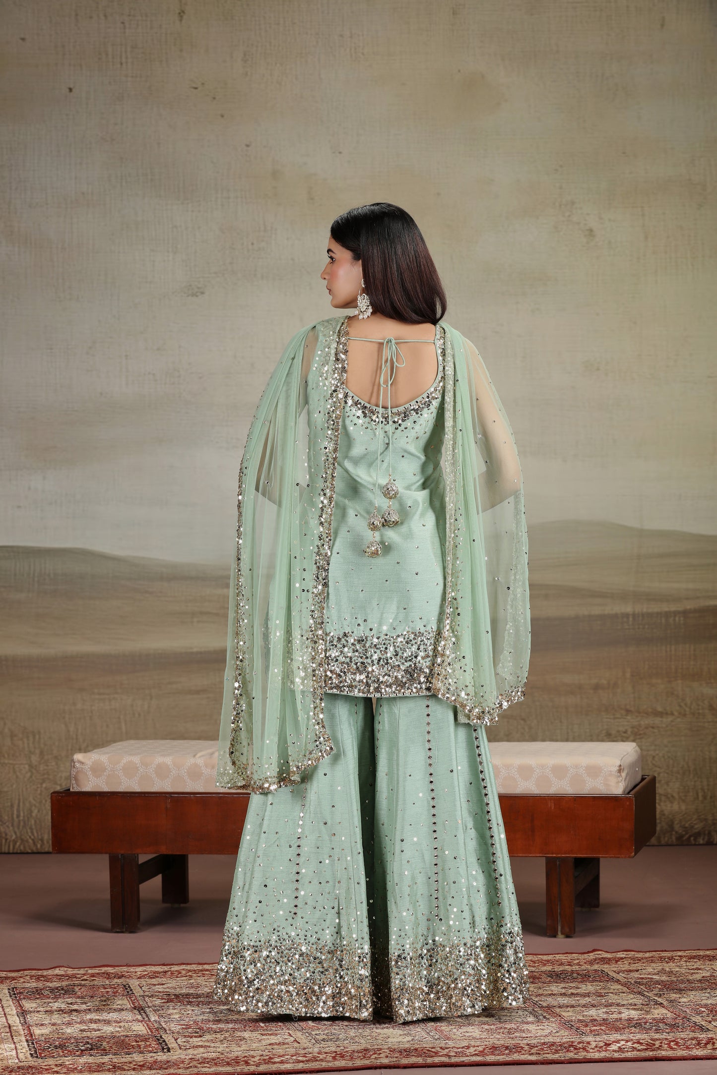 Woman in a light green embroidered traditional outfit standing in a room with a textured wall.