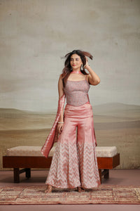 Woman in a peach banarasi suit standing in a room with a textured wall and wooden bench.