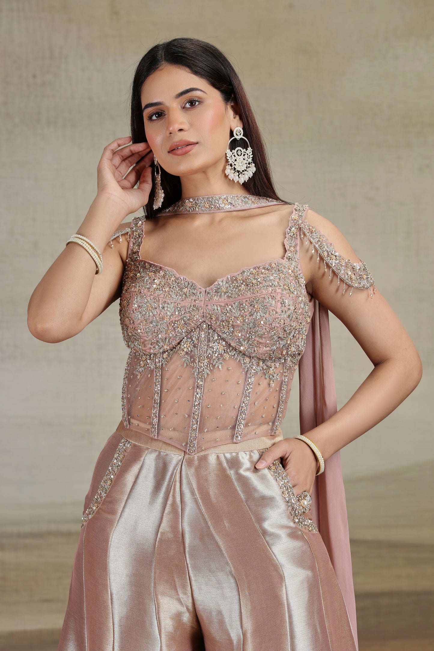 Woman wearing a peach net organza salwar suit with intricate designs and jewelry against a neutral background