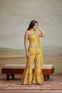 Woman in a yellow organza salwar suit with sequins and thread embroidery standing in front of wooden bench