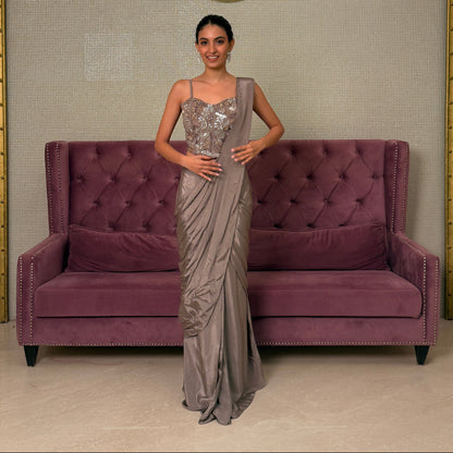 Woman in a silver saree standing next to a purple sofa in a room with a textured wall.