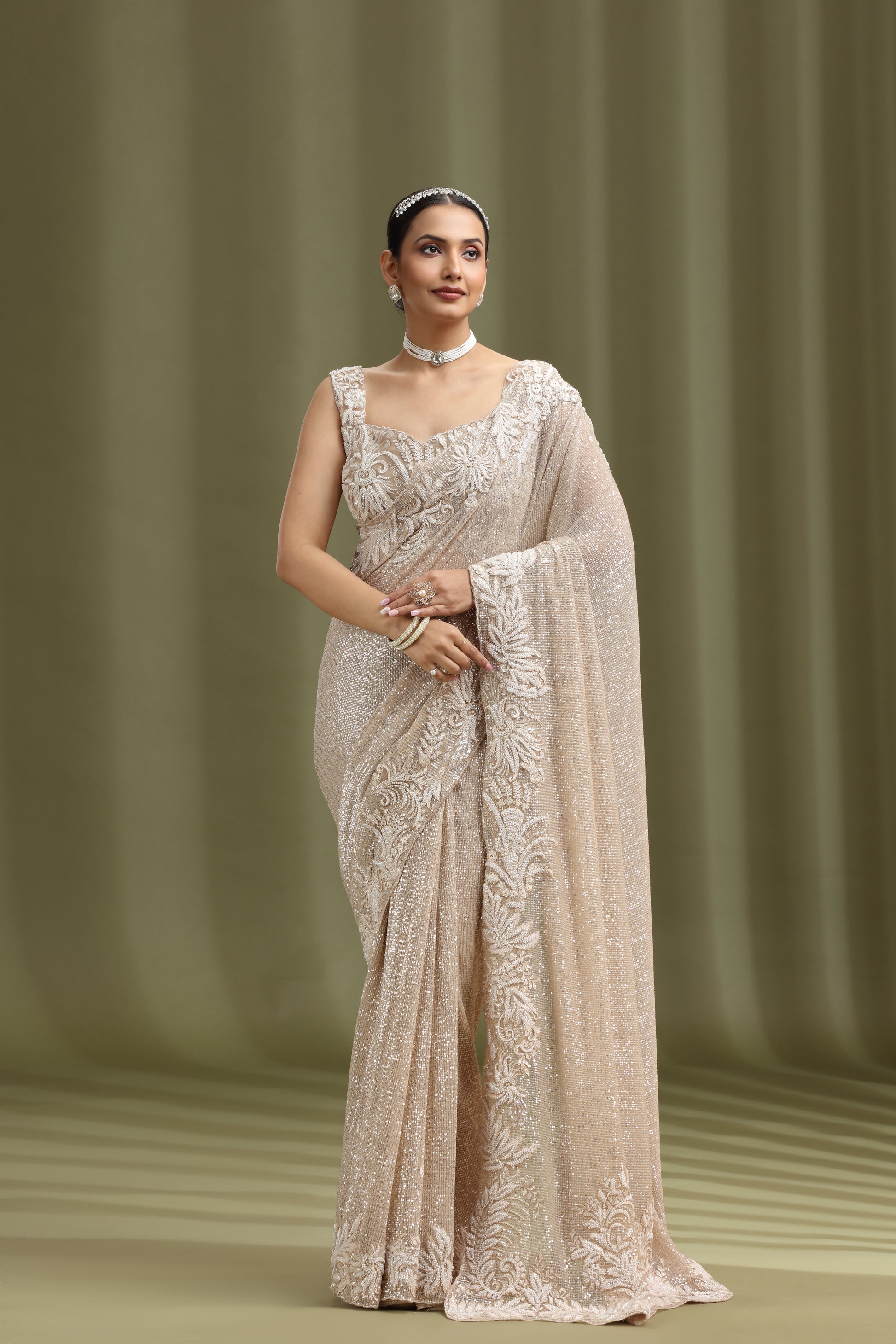 Woman wearing a gold net saree with intricate patterns against a green curtain background