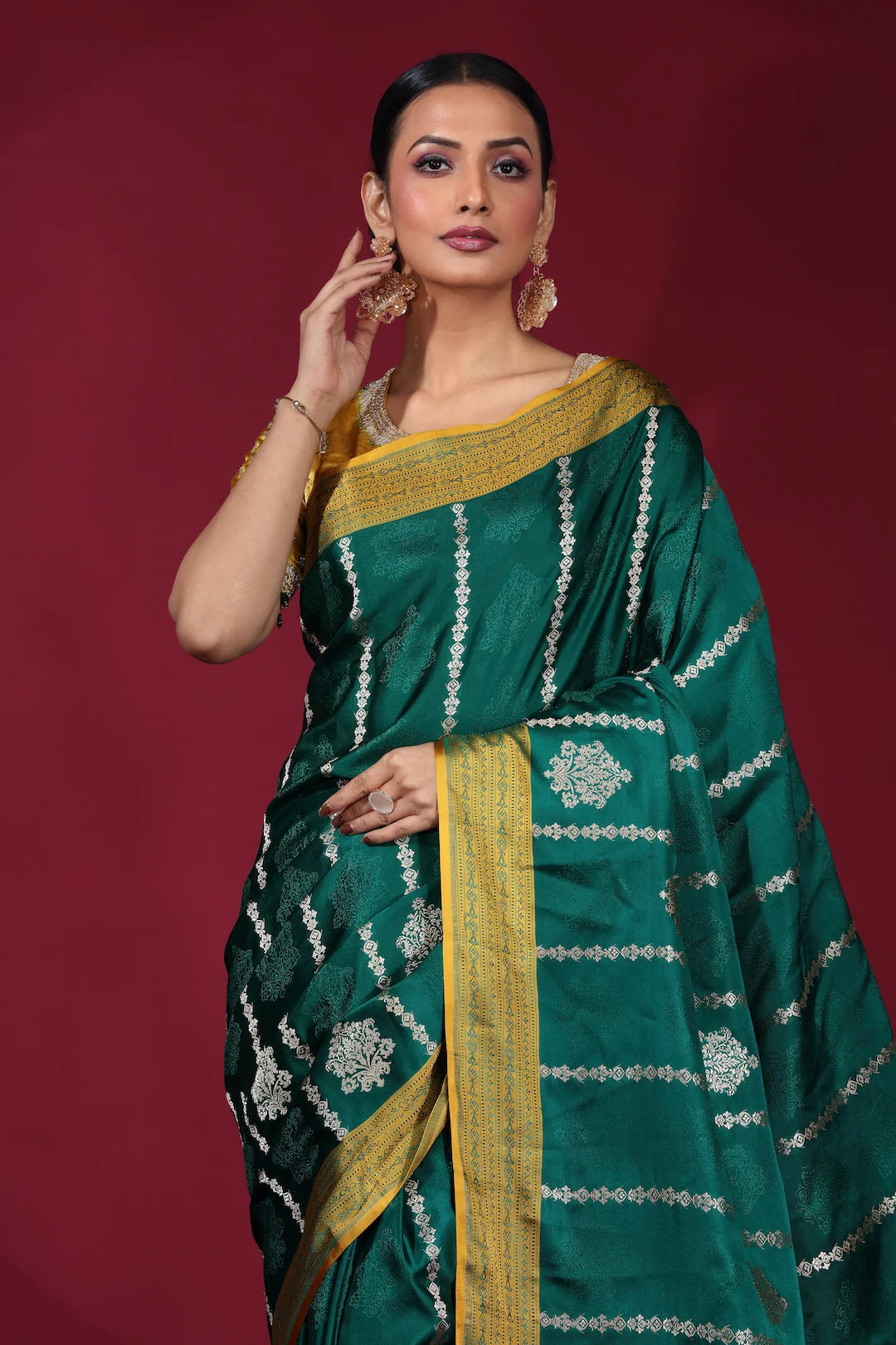 Woman wearing a green saree with gold border against a red background