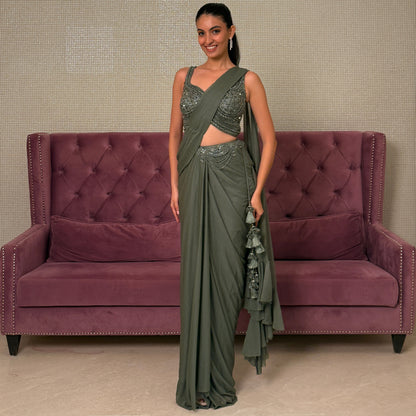 Woman in a green saree standing next to a purple sofa against a beige wall.