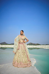 Woman in traditional green raw lehenga standing by a lake with mountains in the background
