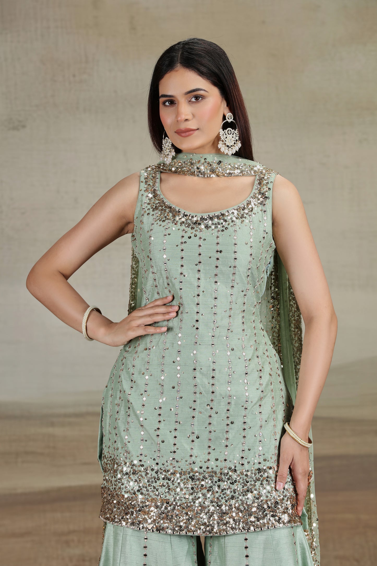 Woman wearing a light green traditional outfit with sequin details against a neutral background