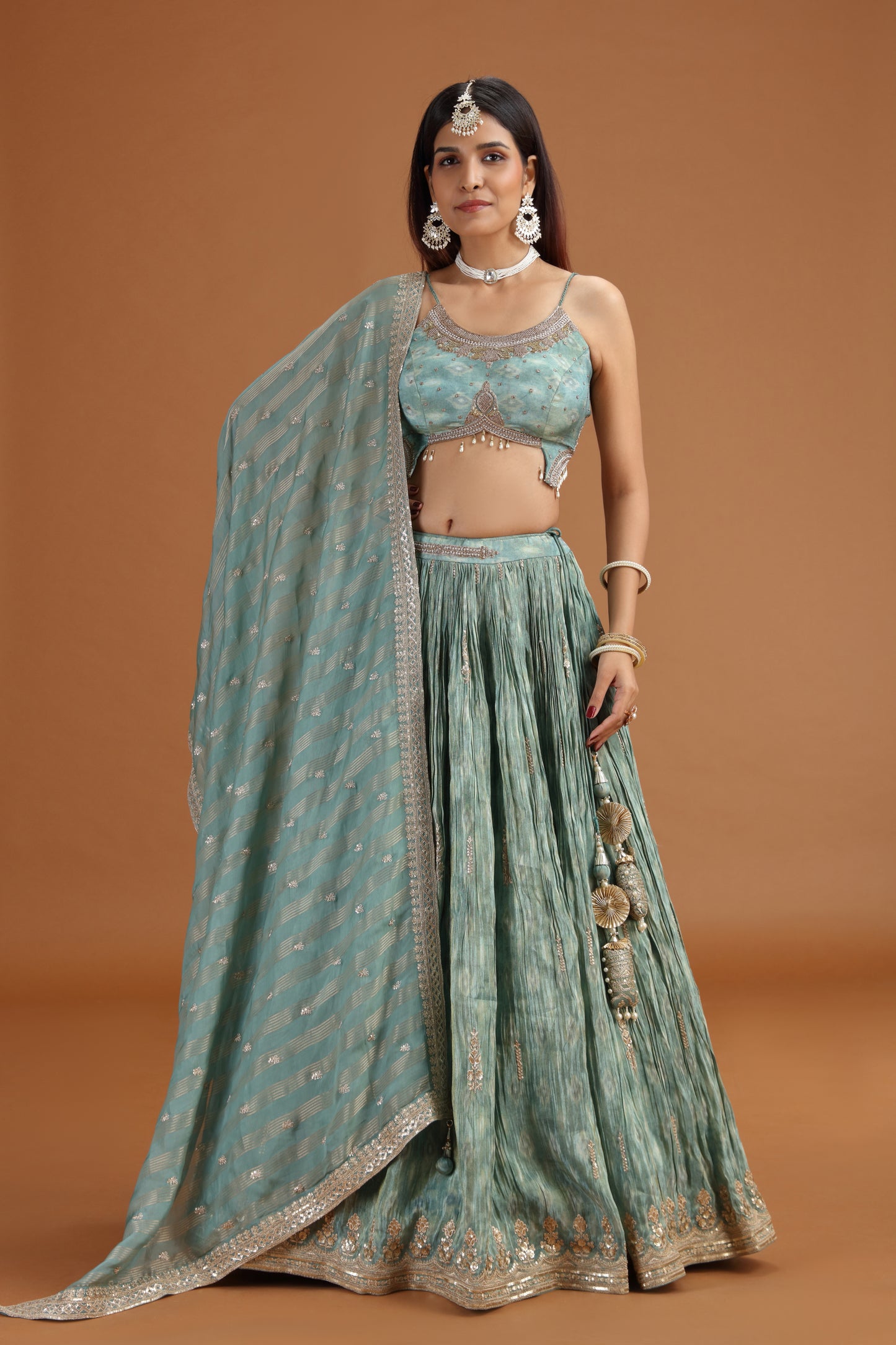 Woman wearing a traditional green and silver outfit with a matching dupatta on a brown background