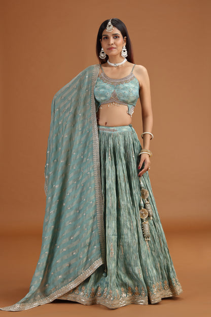 Woman wearing a traditional green and silver outfit with a matching dupatta on a brown background