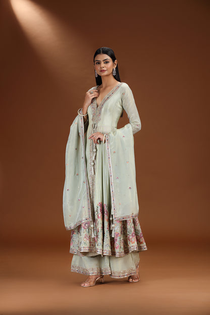 Woman wearing a light green tissue salwar suit with a floral pattern on a brown background