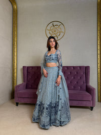 Woman in a blue evening gown standing next to a purple couch in an elegant room.