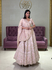 Woman in a pink tissue lehenga standing in a room with a purple couch and decorative wall.