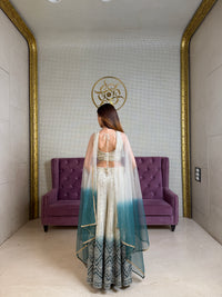 Woman in a long, light-colored dress standing in a room with a purple couch and decorative wall.