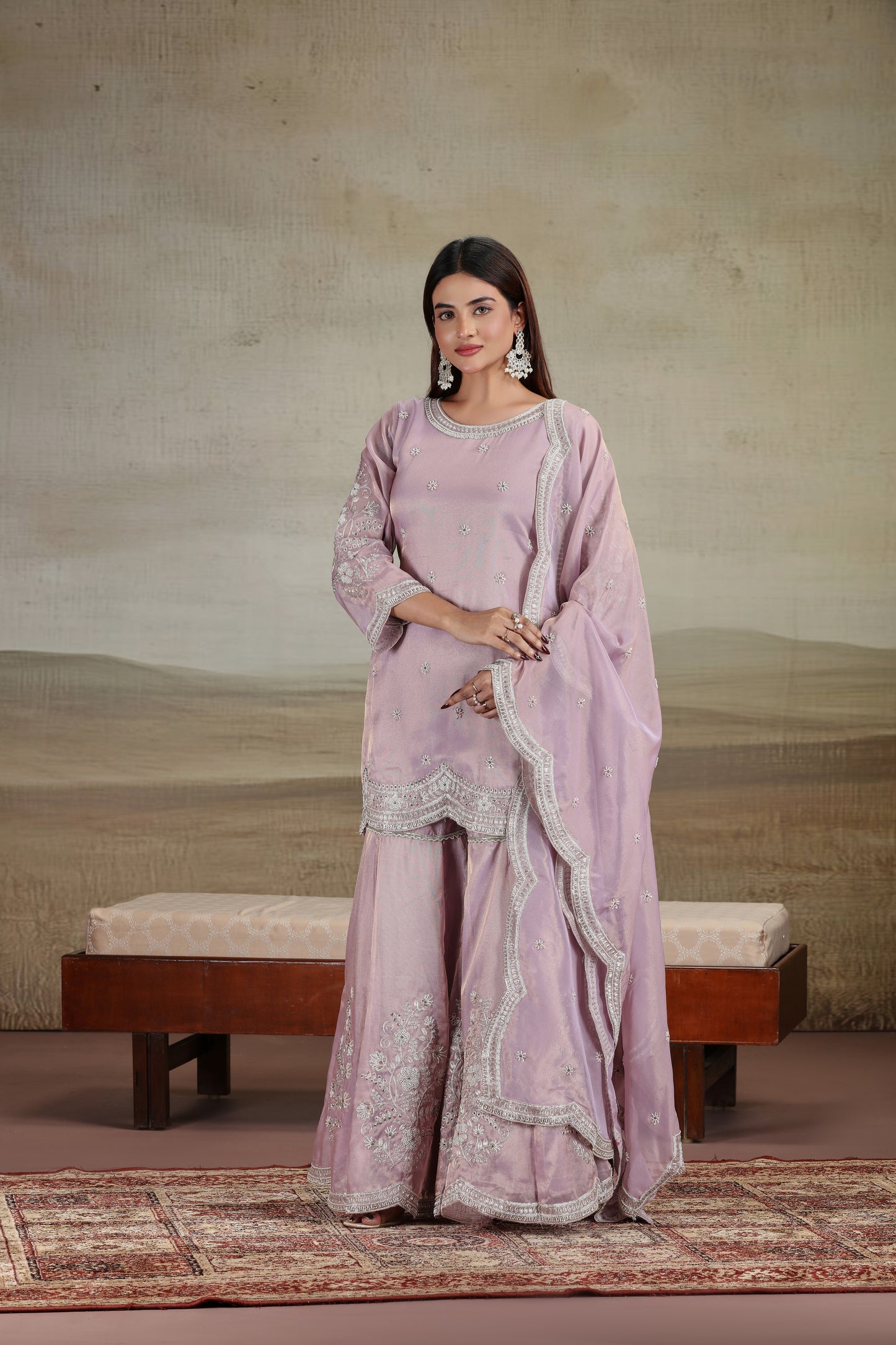 Woman in a lilac suit outfit with embroidery, standing against a neutral background.