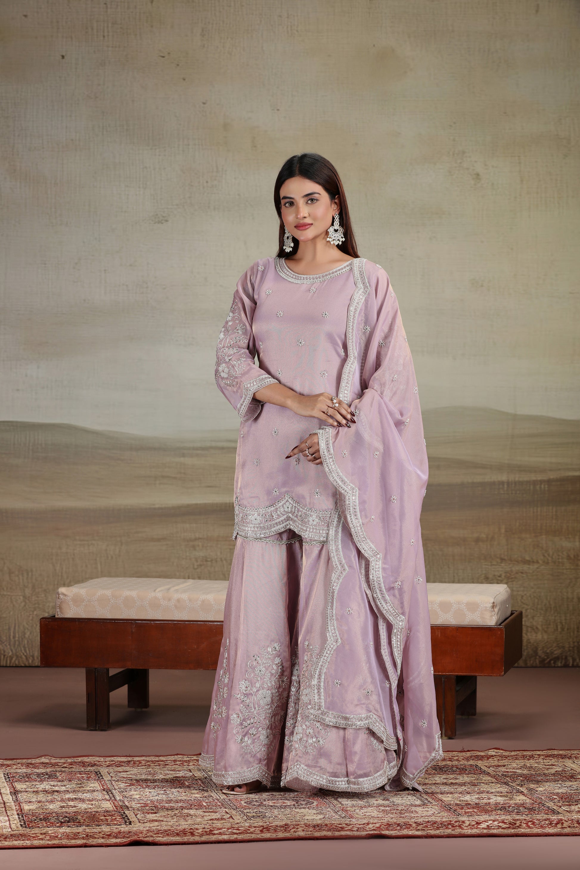 Woman in a lilac suit outfit with embroidery, standing against a neutral background.