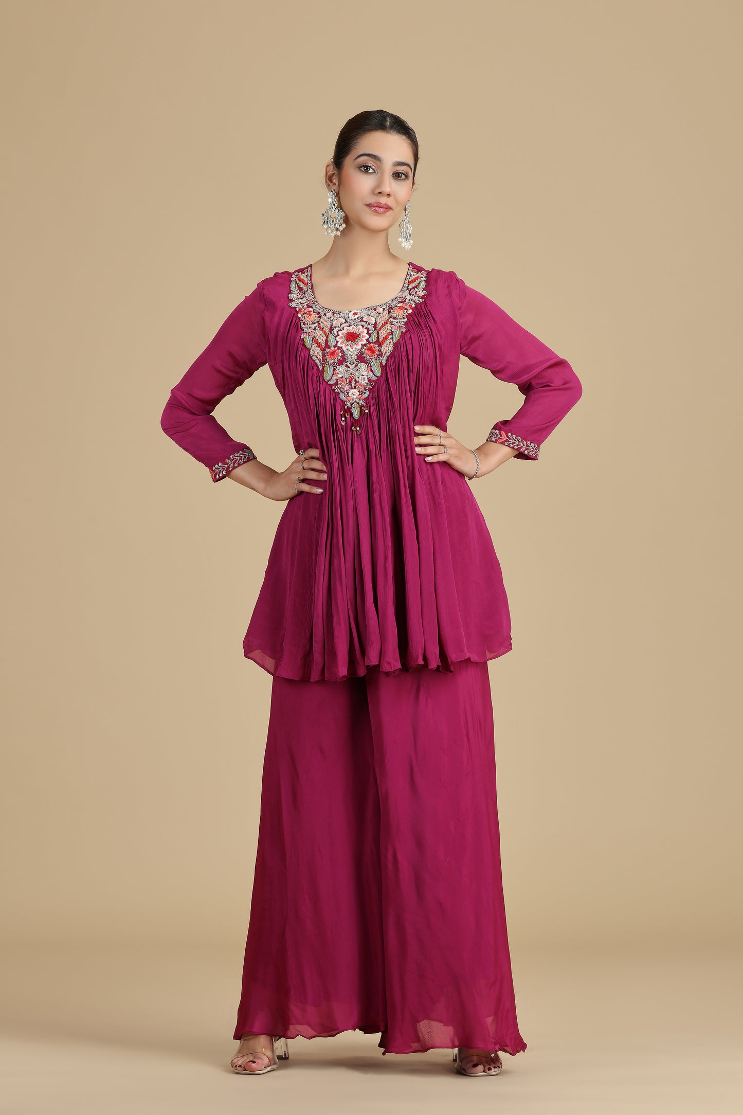 Woman wearing a magenta traditional outfit with intricate embroidery on a beige background