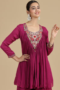 Woman wearing a magenta kurta with intricate embroidery on a beige background