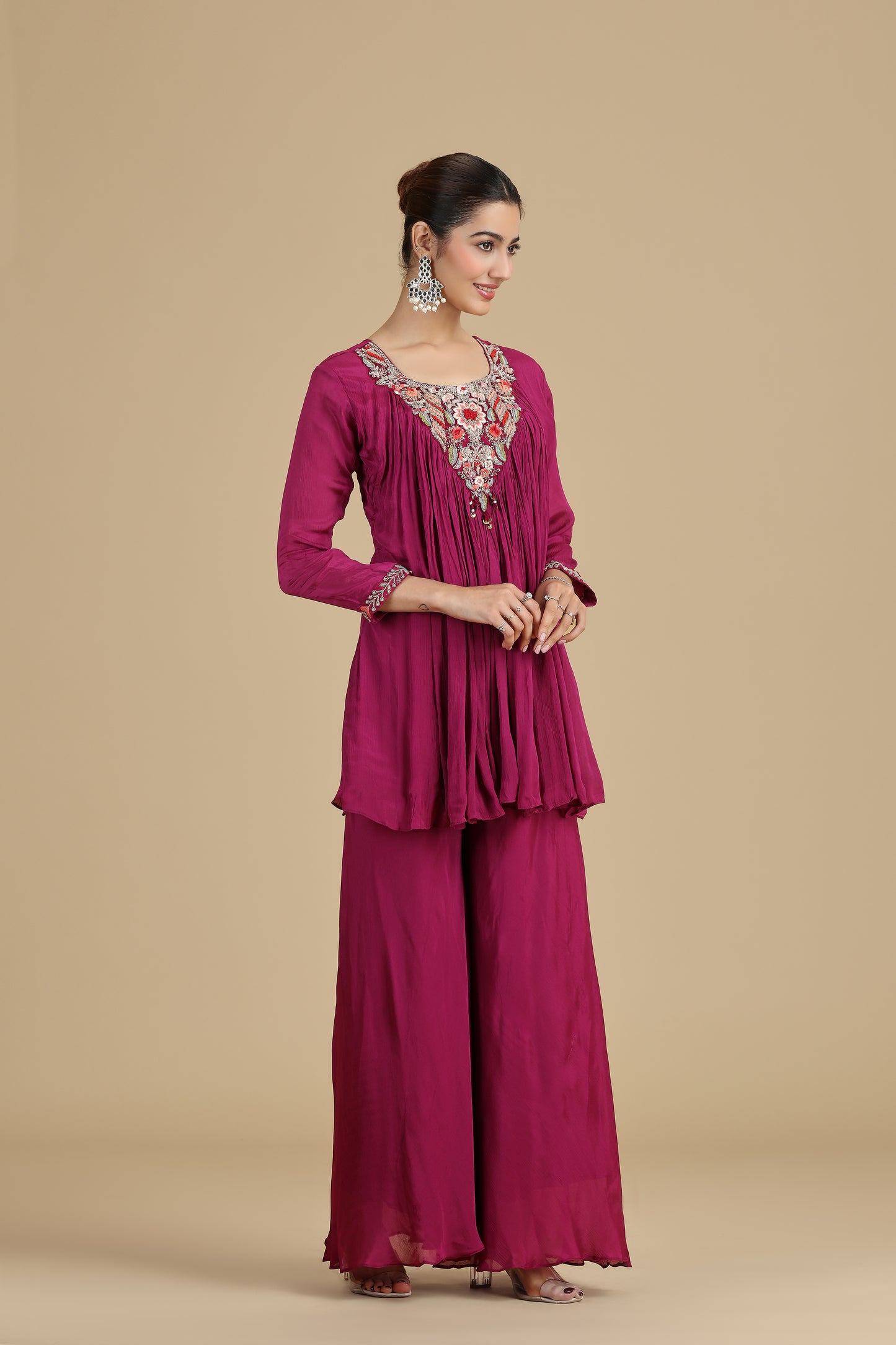 Woman wearing a magenta traditional outfit with intricate detailing on a beige background