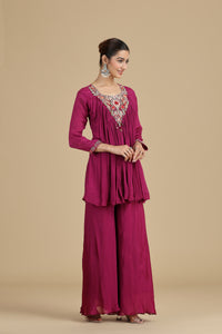 Woman wearing a magenta traditional outfit with intricate detailing on a beige background