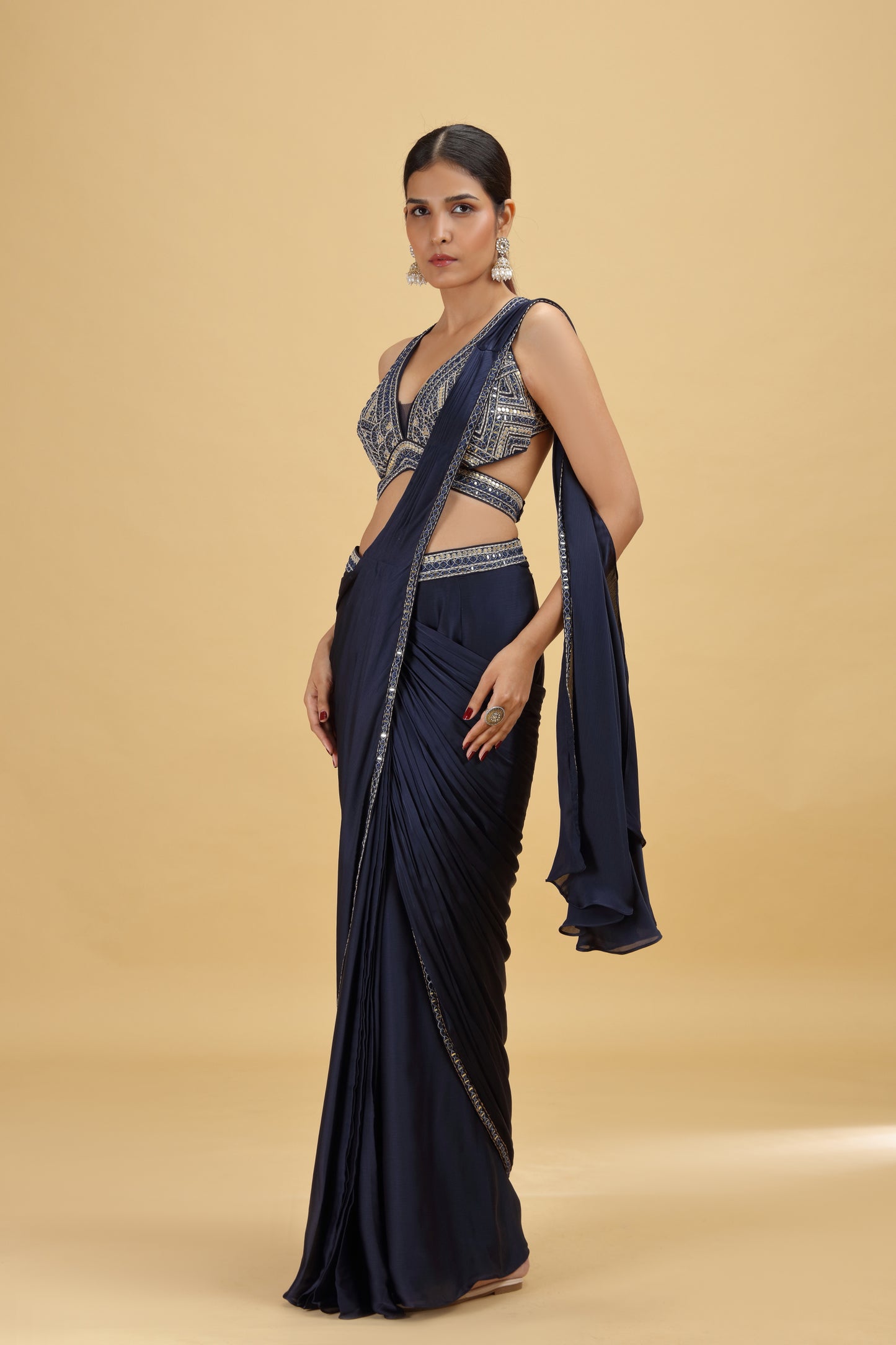 Woman wearing a navy blue saree with a matching blouse on a beige background