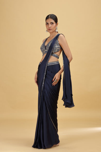 Woman wearing a navy blue saree with a matching blouse on a beige background