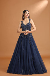 Woman wearing a navy blue evening gown with intricate detailing on a brown background