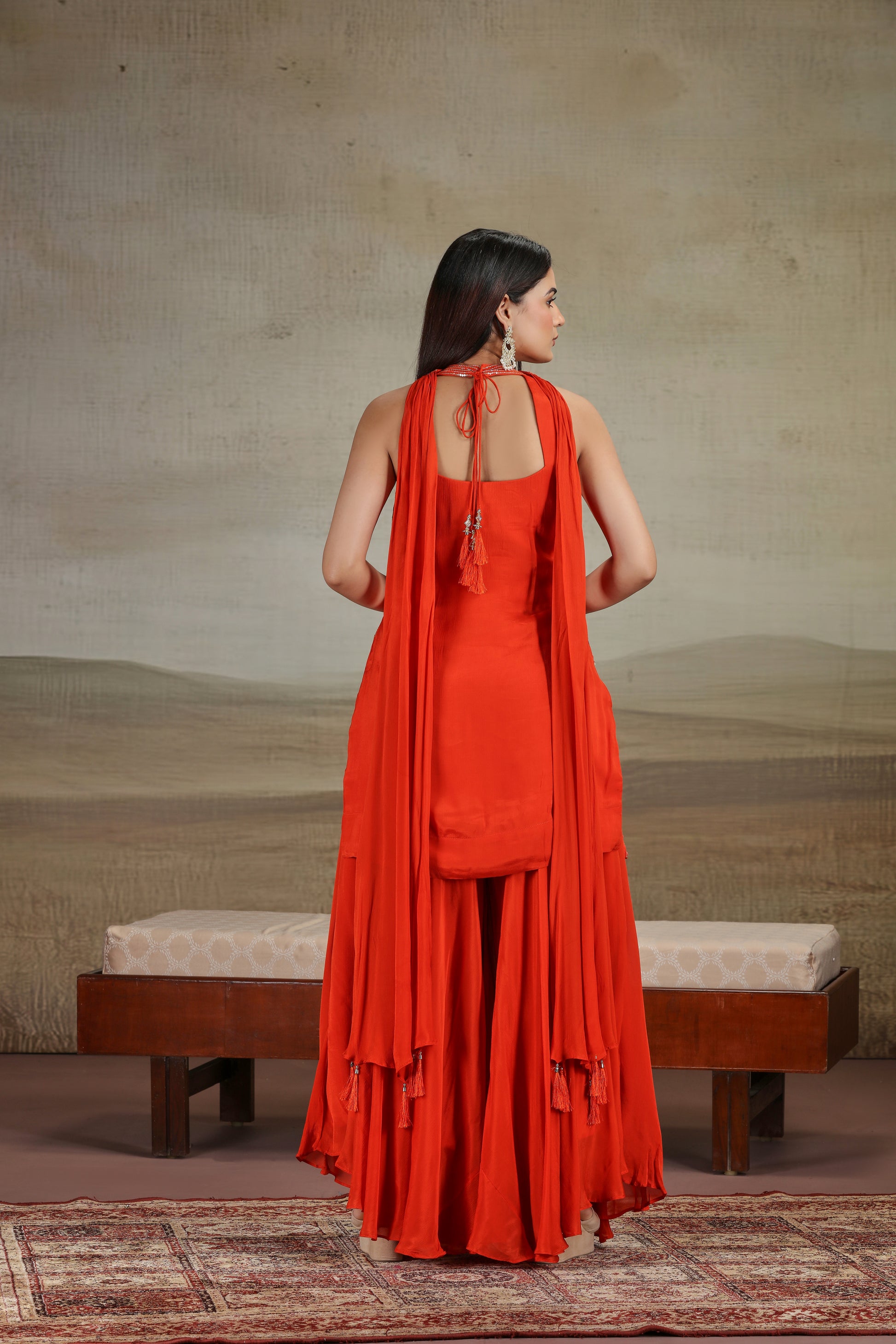 Woman in a red dress standing in front of a textured wall with a wooden bench.