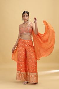 Woman wearing an orange traditional outfit with a dupatta on a beige background