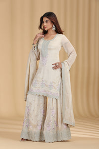 Woman wearing a designer beige tissue salwar suit set with resham and zari work