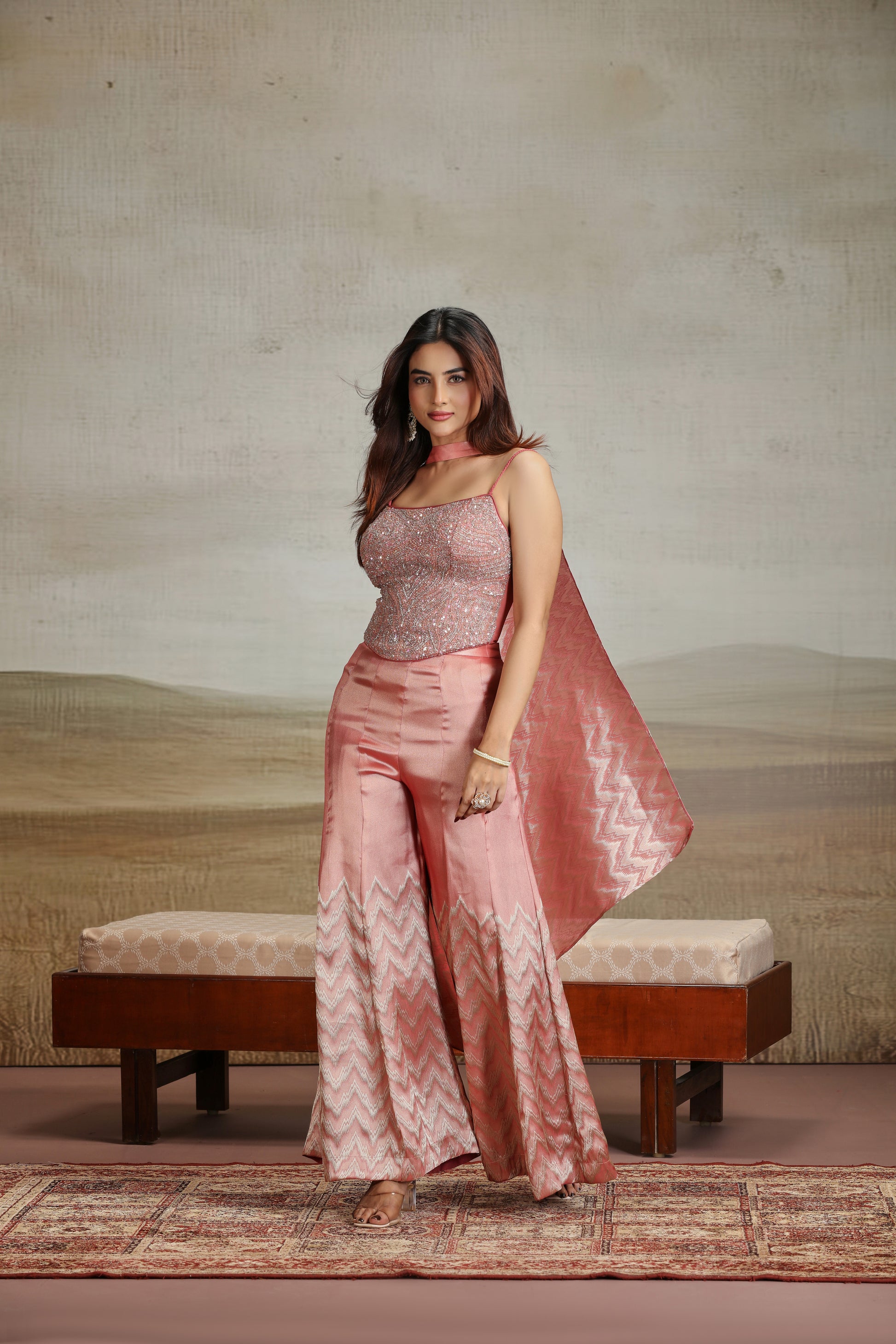 Woman in a peach traditional outfit standing in a room with a textured wall and wooden bench.