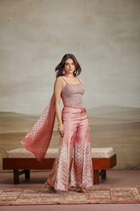 Woman in a peach pink traditional outfit standing in a room with a textured wall and wooden bench.