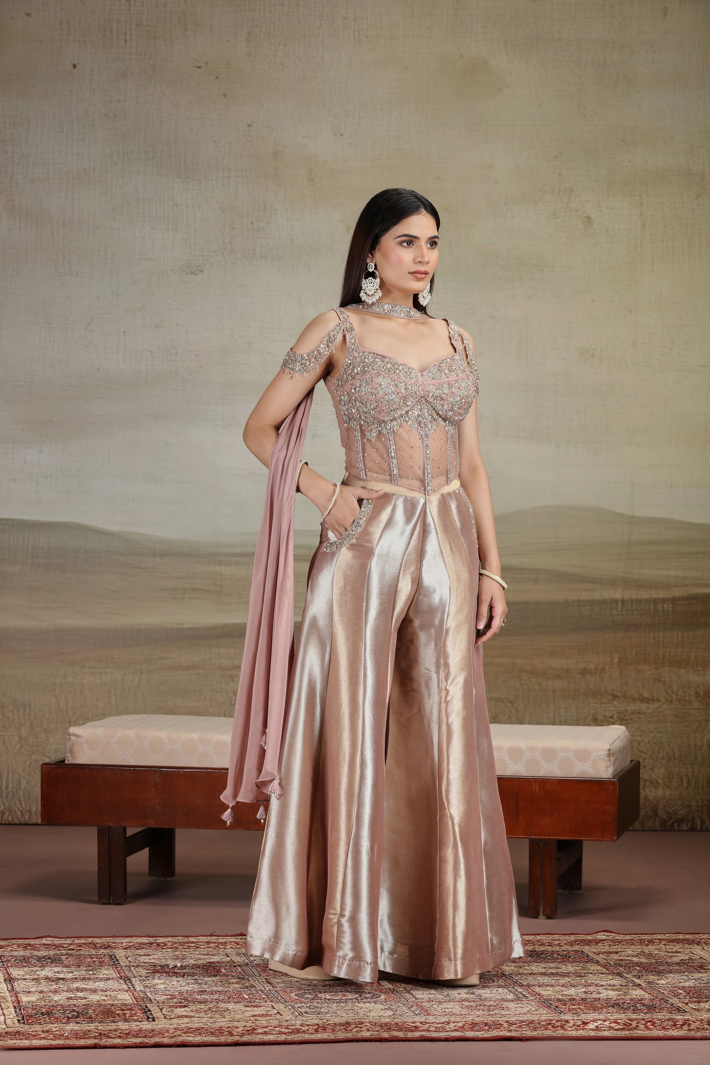 Woman in a peach organza salwar kameez with zari work holding a pink dupatta against a neutral background