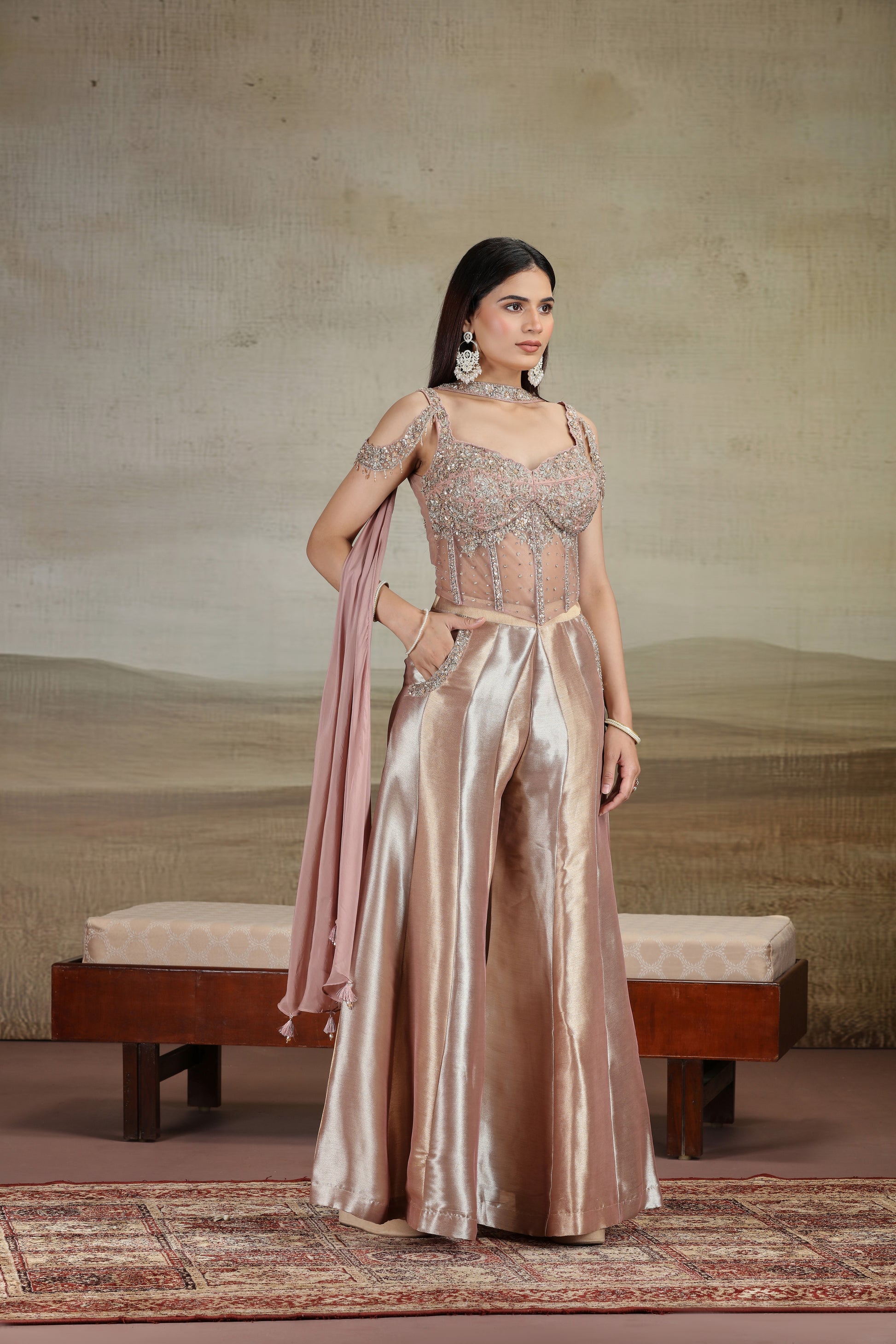 Woman in a peach organza salwar kameez with zari work holding a pink dupatta against a neutral background