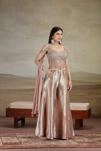 Woman in a peach organza salwar kameez with zari work holding a pink dupatta against a neutral background