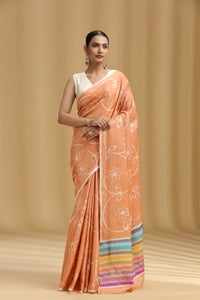 Woman wearing an peach saree with a white blouse against a beige background
