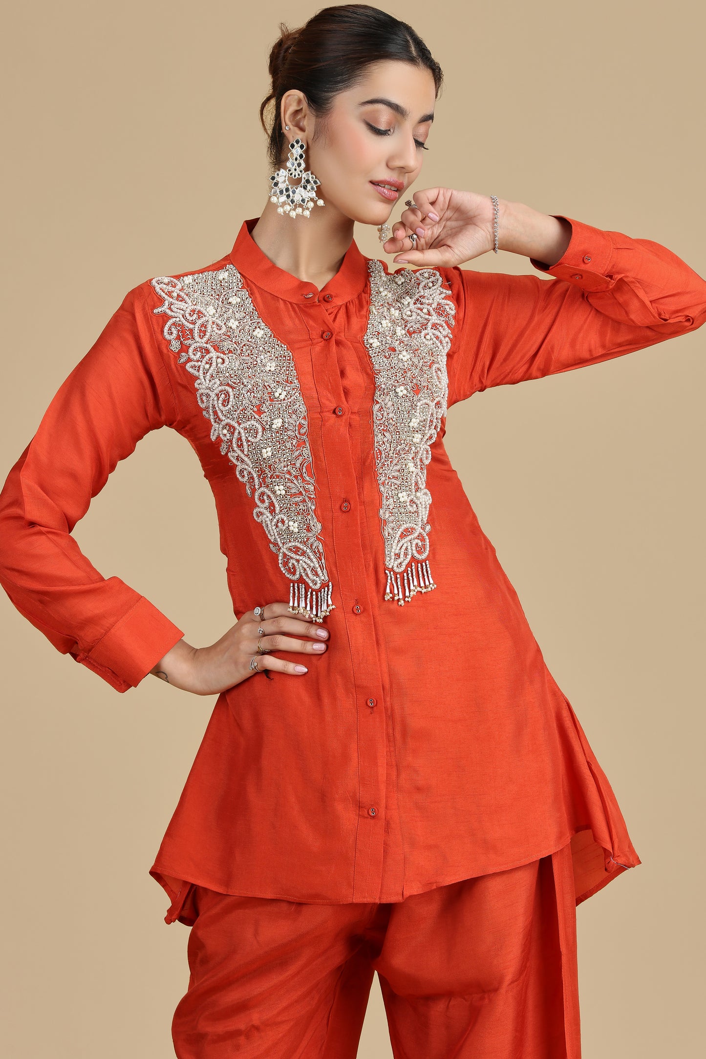 Woman wearing an orange outfit with intricate white embroidery on a beige background