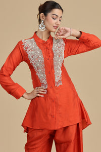 Woman wearing an orange outfit with intricate white embroidery on a beige background