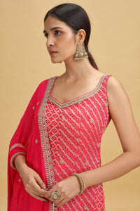 Woman wearing a pink banarasi salwar kameez set with gold embroidery on a beige background