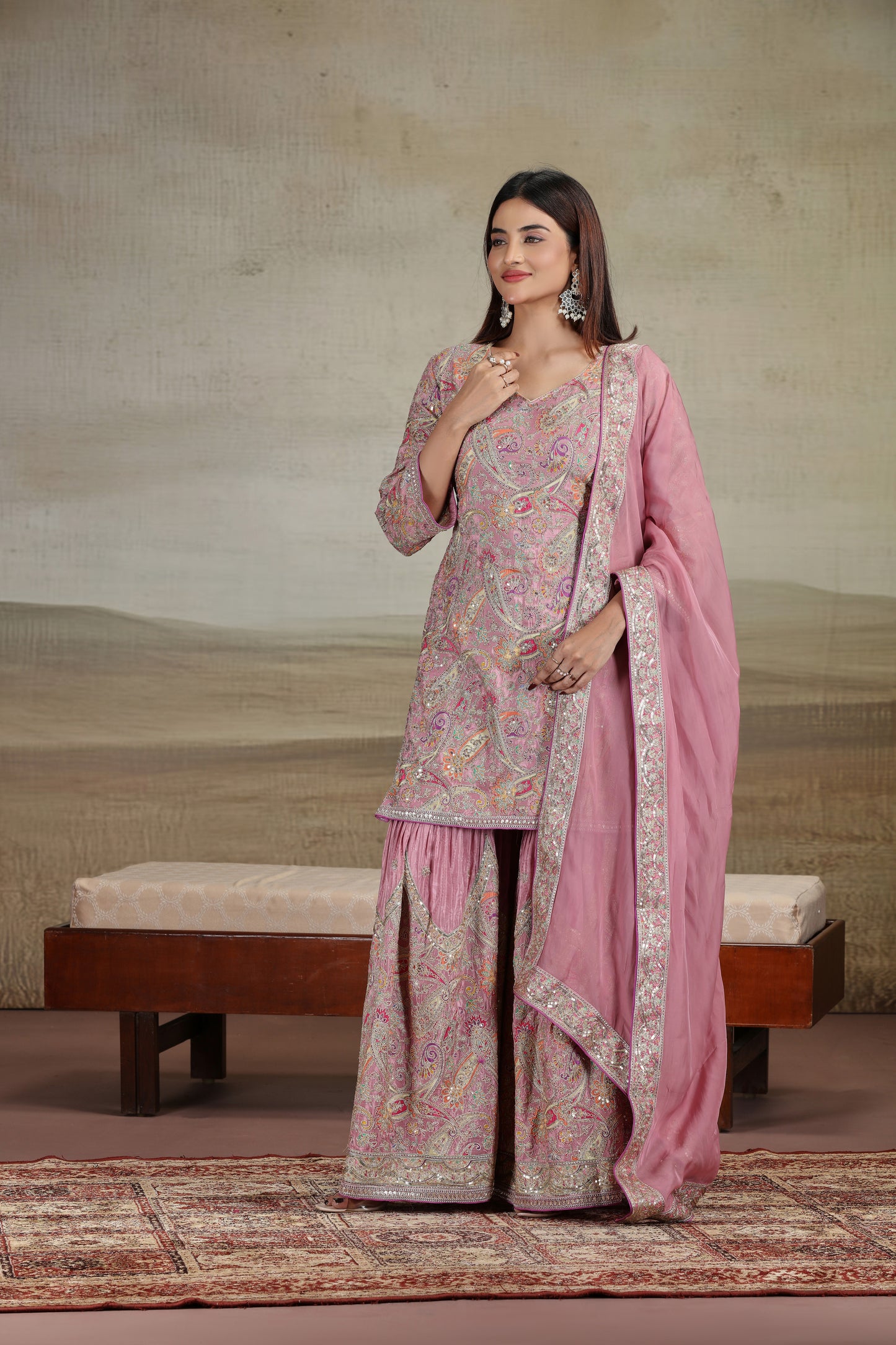 Woman in a traditional pink and beige outfit with a matching dupatta, standing against a neutral background.
