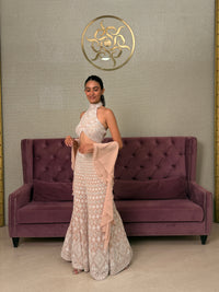Woman in a Pink Salwar Kameez standing next to a purple couch with a decorative wall emblem.