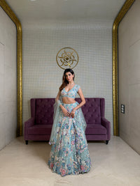 Woman in a floral blue lehenga standing in a room with a purple couch and decorative wall.